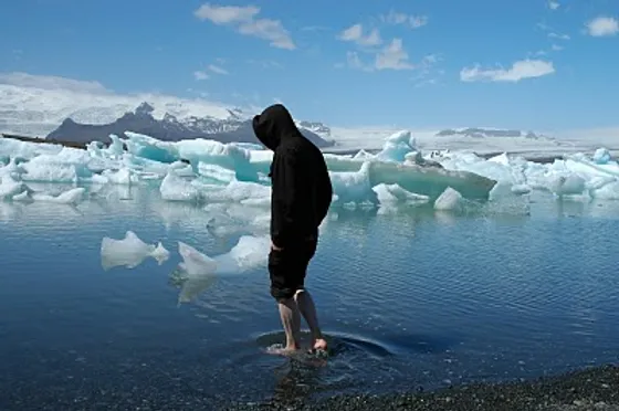 Person wading in the icy waters of Jökulsárlón Glacier Lagoon in Iceland, surrounded by floating icebergs under a clear blue sky.