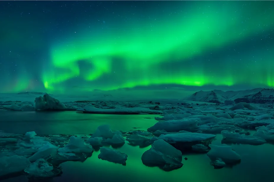 Stunning Northern Lights illuminating the sky over Jökulsárlón Glacier Lagoon in Iceland, with floating icebergs and a serene, reflective water surface.