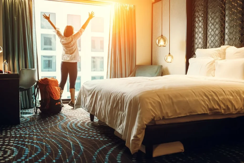 A traveler standing in a bright hotel room near Keflavik International Airport, Iceland, stretching with excitement as sunlight fills the room.