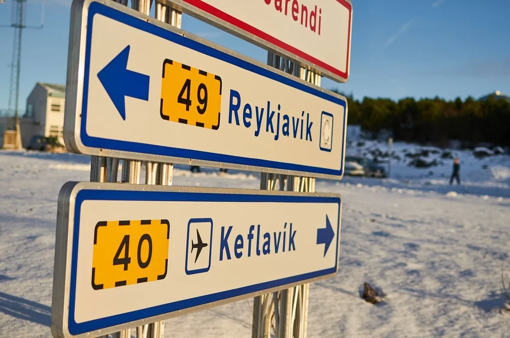 Directional road signs indicating the routes to Reykjavik and Keflavik Airport in Iceland, with a snowy landscape in the background.