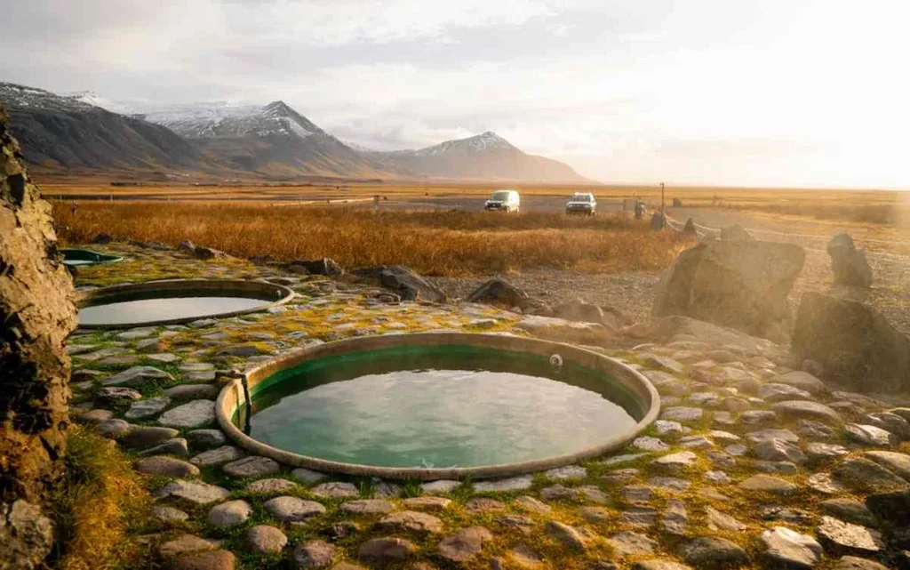 Natural hot tubs at Hoffell in Iceland, surrounded by a stunning landscape of mountains and open fields during a golden sunset.