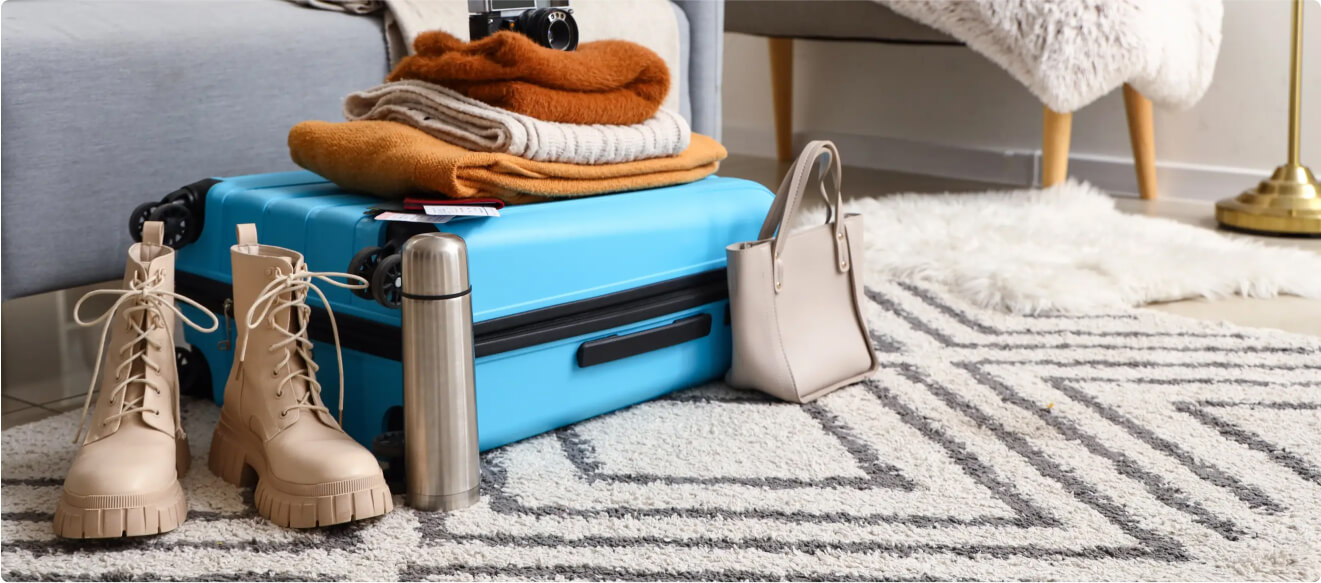 Open suitcase with winter clothing, boots, and travel essentials including a bag and a camera