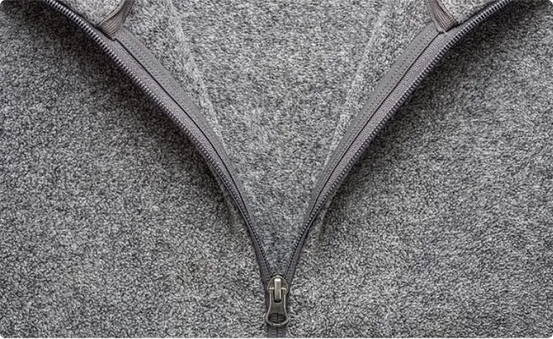 Close-up of a gray fleece jacket zipper, showcasing a warm and breathable second layer essential for Iceland travel.