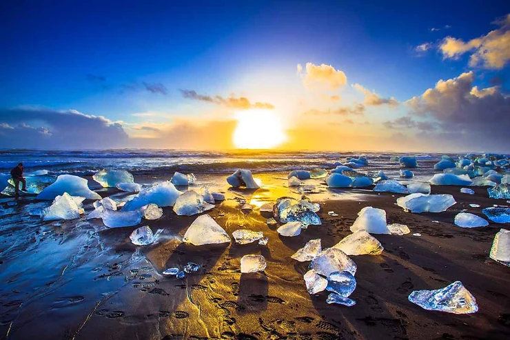 Scenic view of icebergs glistening on the black sand beach at Skaftafell, Iceland, during a vibrant sunrise.