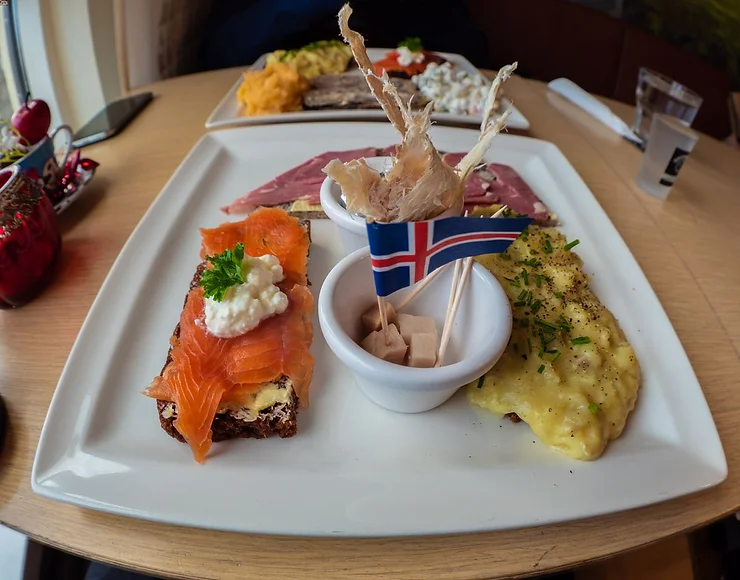 Traditional Icelandic food platter featuring hákarl (fermented shark meat) with an Icelandic flag, smoked salmon, and other local delicacies.