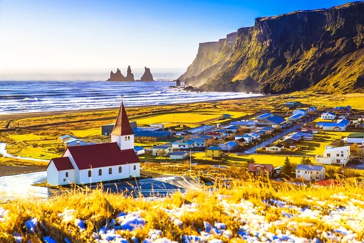 Picturesque view of the town of Vík í Mýrdal with its iconic church, red roof, and the dramatic Reynisdrangar sea stacks in the background.