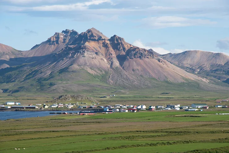 A small town of Bakkagerði in Iceland, situated at the base of rugged, jagged mountains under a clear sky.