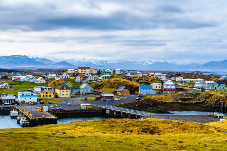 A picturesque view of Stykkisholmur town with colorful houses, a small harbor, and snow-capped mountains in the background, Iceland.