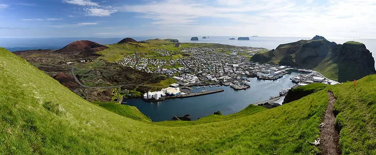 Panoramic view of Vestmannaeyjabaer, the main town on the Westman Islands, Iceland, with lush green hills and the harbor in the foreground.