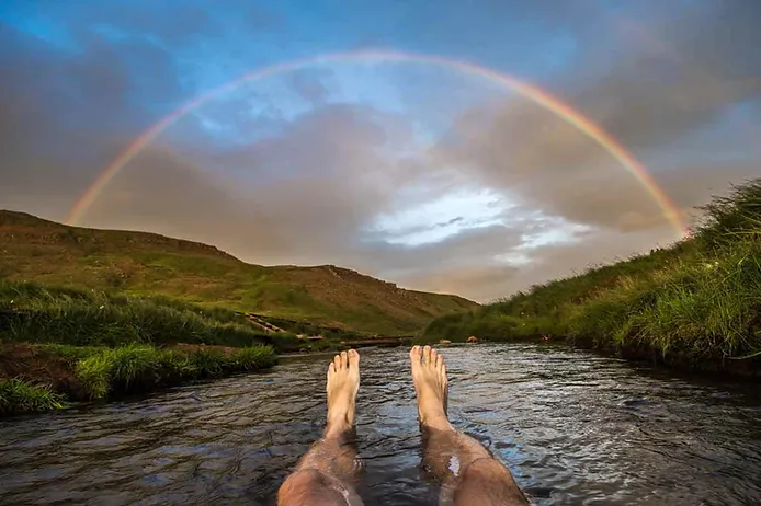 Person relaxing in Reykjadalur hot springs under a rainbow in Iceland