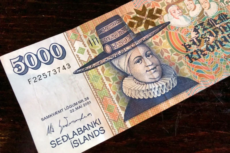 A close-up of a 5000 Icelandic krona banknote, featuring intricate patterns and the portrait of a historical figure wearing a traditional hat, with the text 