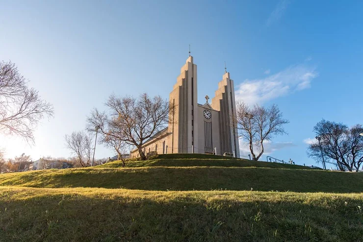 Akureyri Church, an iconic modernist architectural landmark, bathed in sunlight and standing atop a hill in Akureyri, Iceland.