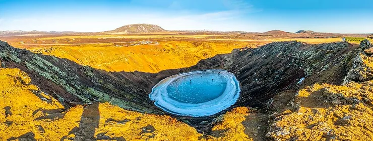 A panoramic view of Kerid Crater in Iceland, showcasing its stunning volcanic landscape with a partially frozen lake at the bottom, part of the Golden Circle route.