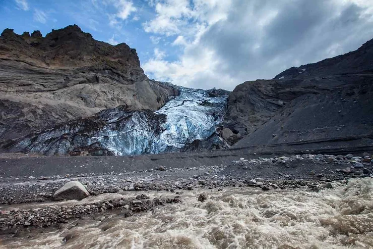 Glacial ice melting and flowing into a turbulent river at the base of Eyjafjallajökull volcano in Iceland, with rugged cliffs in the background.