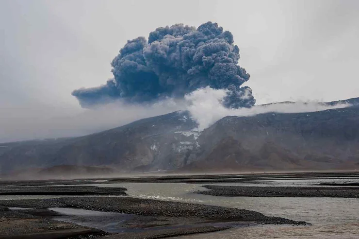 The Eyjafjallajökull volcano in Iceland erupting, sending a massive plume of ash and smoke into the sky over a desolate landscape.