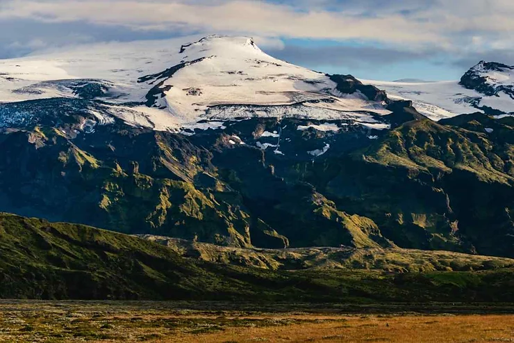 The majestic Eyjafjallajökull volcano in Iceland, covered in snow, with lush green landscapes at its base under a clear sky.