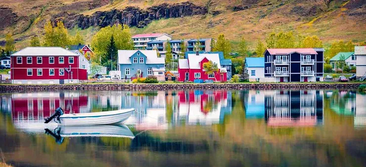 Colorful houses reflected in the calm waters of Seyðisfjörður, Iceland, with a small boat anchored near the shore.