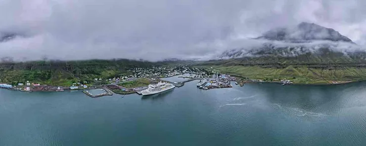 Aerial panoramic view of Seyðisfjörður, a picturesque coastal town in Iceland, surrounded by misty mountains and calm waters.