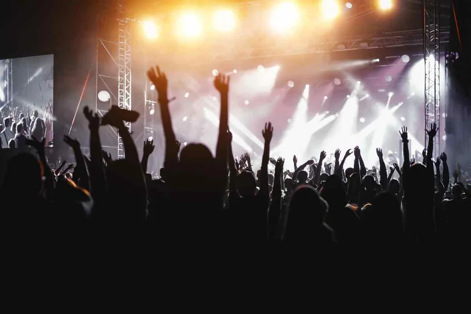 Silhouettes of a crowd with raised hands at a concert, with bright stage lights and an energetic atmosphere, capturing the excitement of a live music event