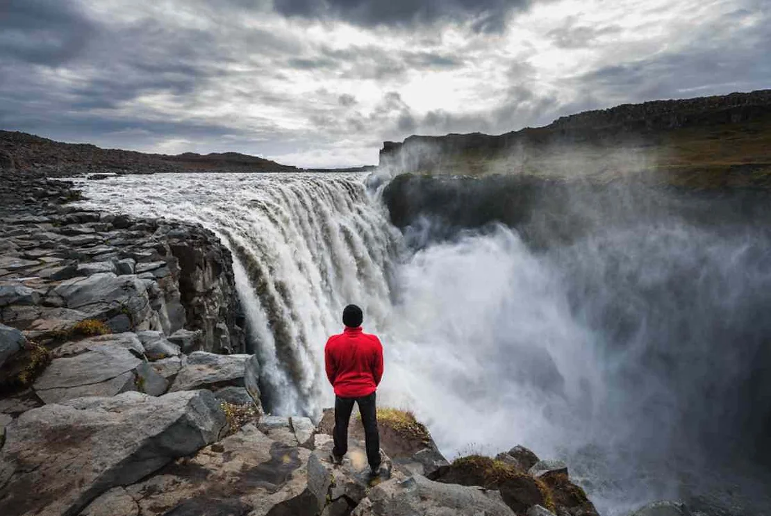 Man standing right by the powerful dettiffoss waterfall in Iceland