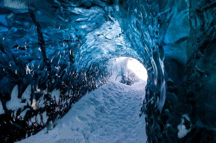 A stunning ice cave with blue walls and a snowy path leading through it, located near Vik, Iceland.