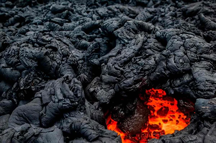 A vivid display of cooling lava with glowing orange magma visible beneath the hardened black crust in Iceland.