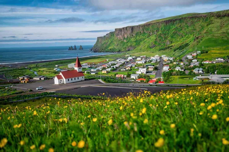 Scenic view of the town of Vik in Iceland, with its iconic red-roofed church and the dramatic cliffs in the background.