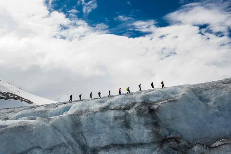 Group of hikers walking in a line on a glacier near Vik, Iceland, under a bright blue sky with clouds.