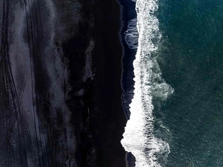 A stunning aerial photograph of Vík’s black sand beach in Iceland, with dark sand contrasting against the white surf of the Atlantic Ocean