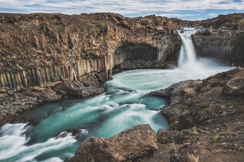 Aldeyjarfoss waterfall in Iceland, featuring powerful water flow over basalt columns into a turquoise pool, surrounded by rugged volcanic landscapes