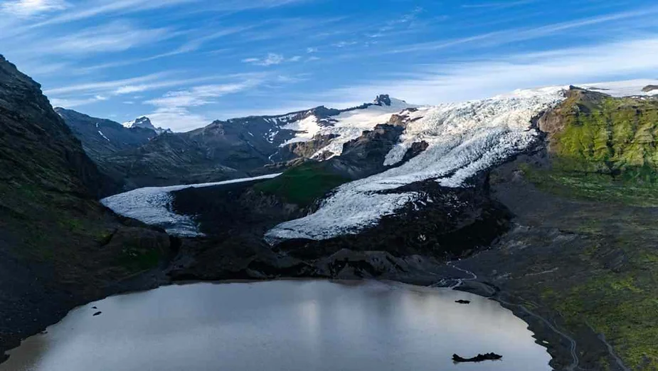 Glacial landscape with a large glacier flowing into a serene lake, surrounded by rugged mountains under a clear blue sky.