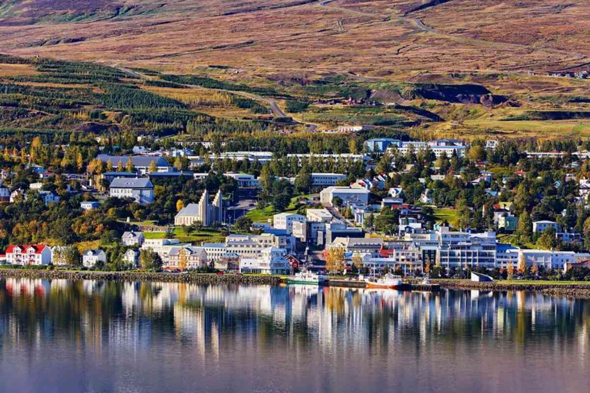 Charming coastal town with colorful buildings reflected in the calm waters, surrounded by rolling hills and greenery.