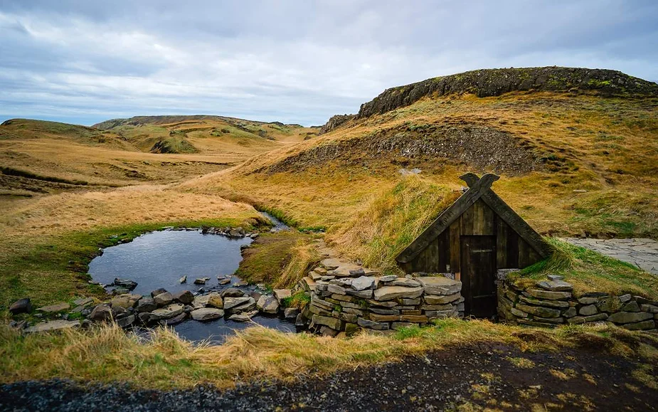 A traditional Icelandic turf house surrounded by rolling hills and a small pond, showcasing the unique architectural style amidst a scenic landscape