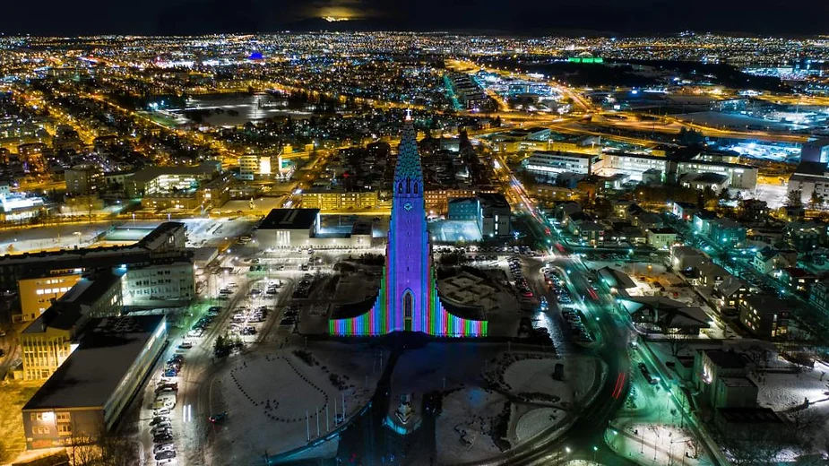 Aerial view of Reykjavik at night, featuring the illuminated Hallgrímskirkja Church with vibrant lights, surrounded by the city's bustling streets and glowing skyline