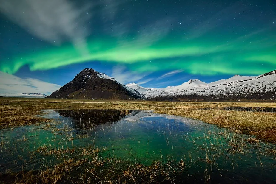 Stunning display of the Northern Lights over snow-capped mountains and a serene water reflection in Iceland's wilderness