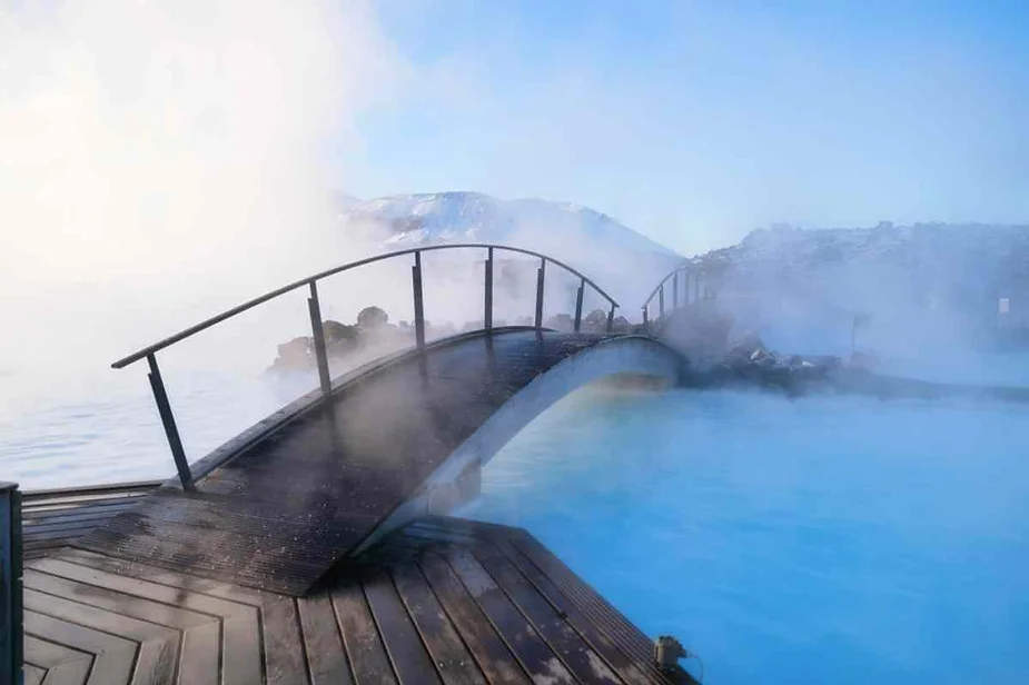 Steamy Blue Lagoon geothermal spa in Iceland with a wooden bridge arching over the milky blue waters under a clear sky.