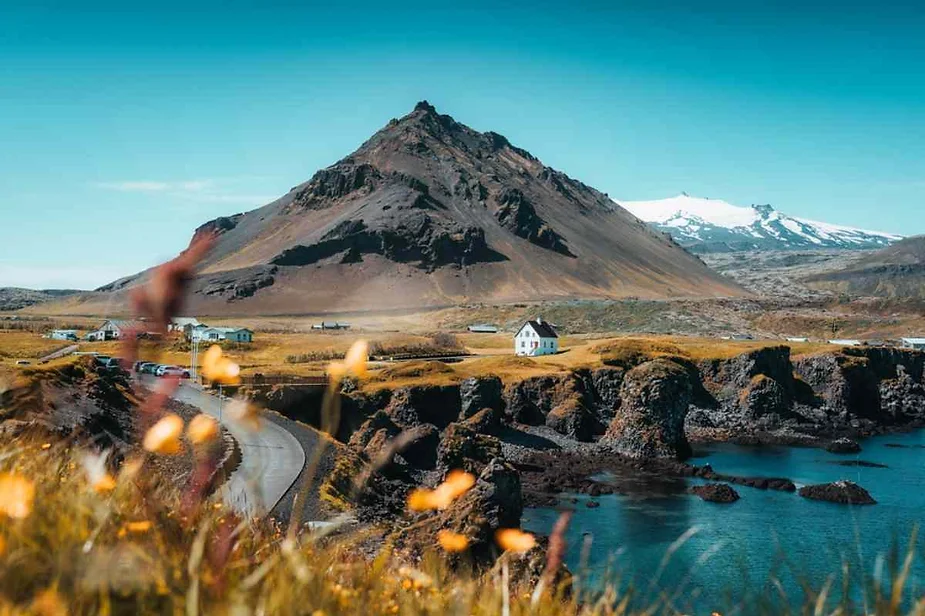 Scenic coastal village in Iceland with a charming white house, rugged cliffs, and a towering mountain in the background on a clear day.