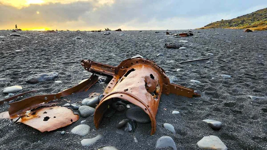 Rusty metal wreckage scattered on a black sand beach in Iceland during a dramatic sunset.