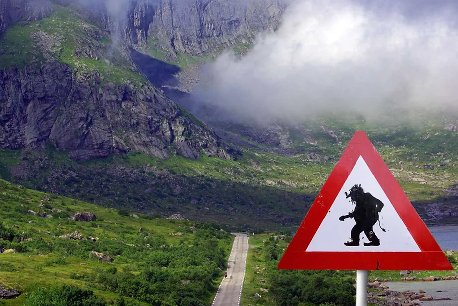 Warning sign with a troll silhouette, set against the backdrop of Iceland's lush green mountains and cloudy sky, indicating a troll crossing