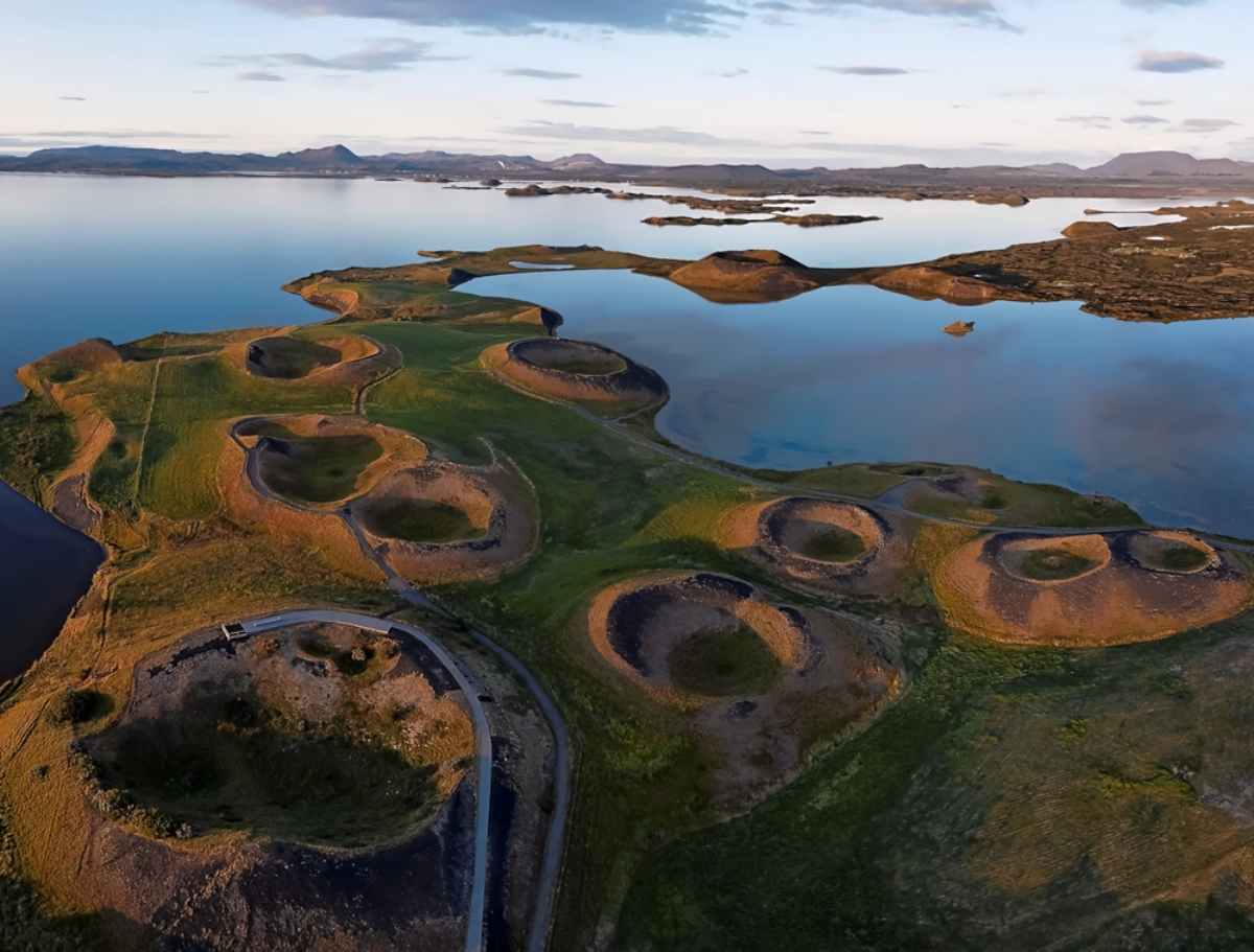 Aerial view of Skútustaðagígar, a series of pseudocraters located by Lake Mývatn in Iceland, with calm waters and distant mountains under a clear sky.