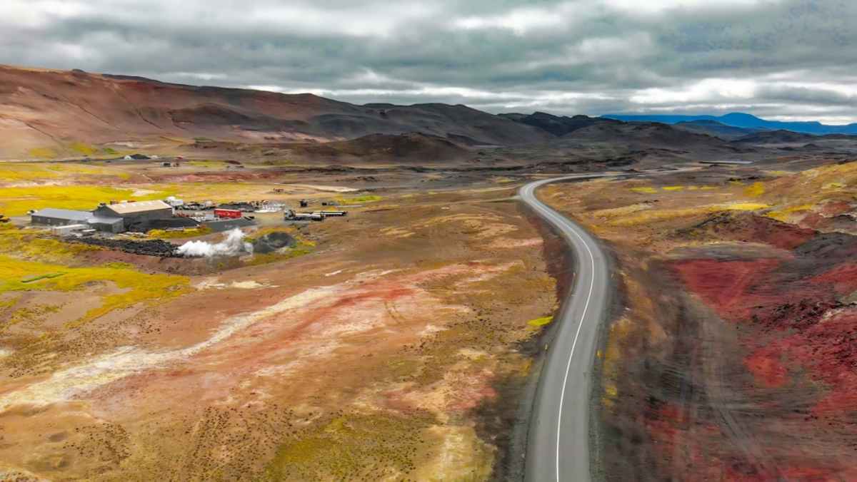 Geothermal power plant releasing steam near Lake Mývatn in Iceland, with a volcanic landscape and clear blue skies in the background.