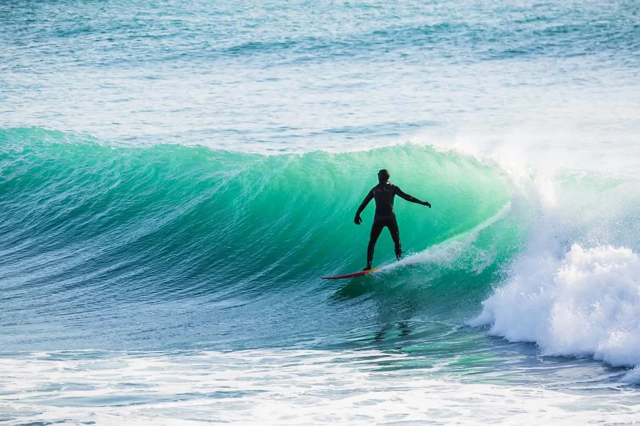 A surfer riding a turquoise wave in the cold waters of Iceland, wearing a wetsuit and displaying expert balance on the board