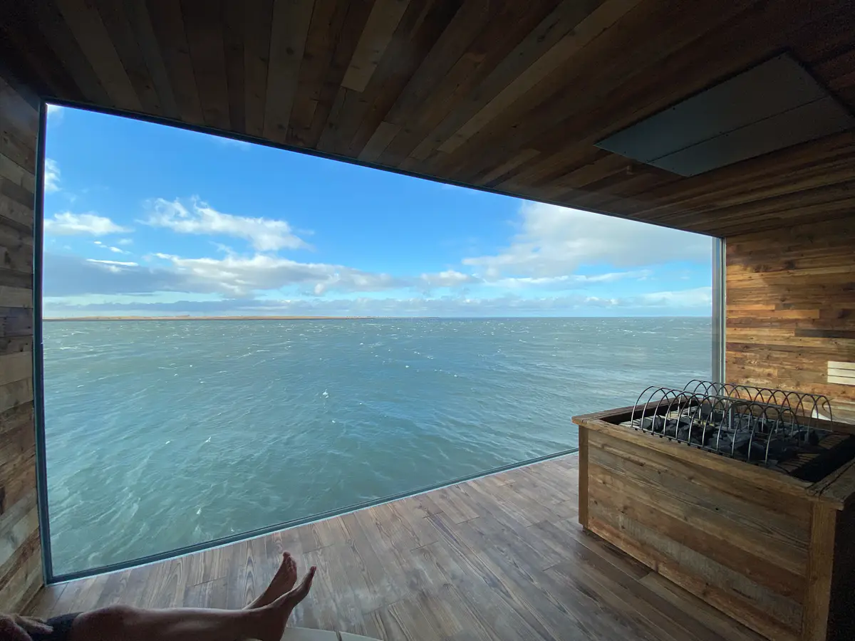 Inside the Sky Lagoon spa in Iceland, featuring panoramic ocean views through a large window and a rustic, wood-clad interior.