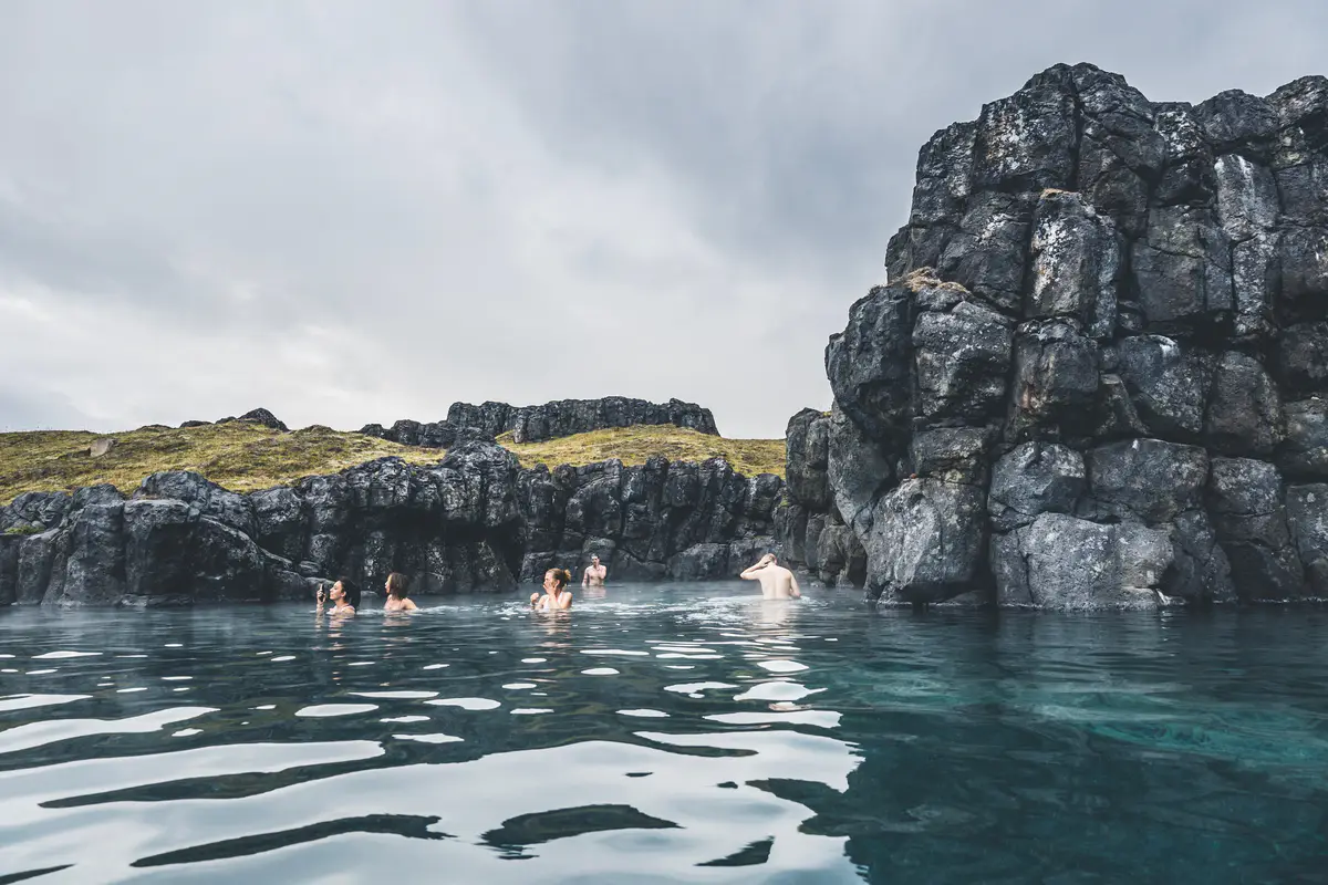 People relaxing in the Sky Lagoon geothermal pool, surrounded by rugged volcanic cliffs and serene waters near Reykjavik, Iceland.