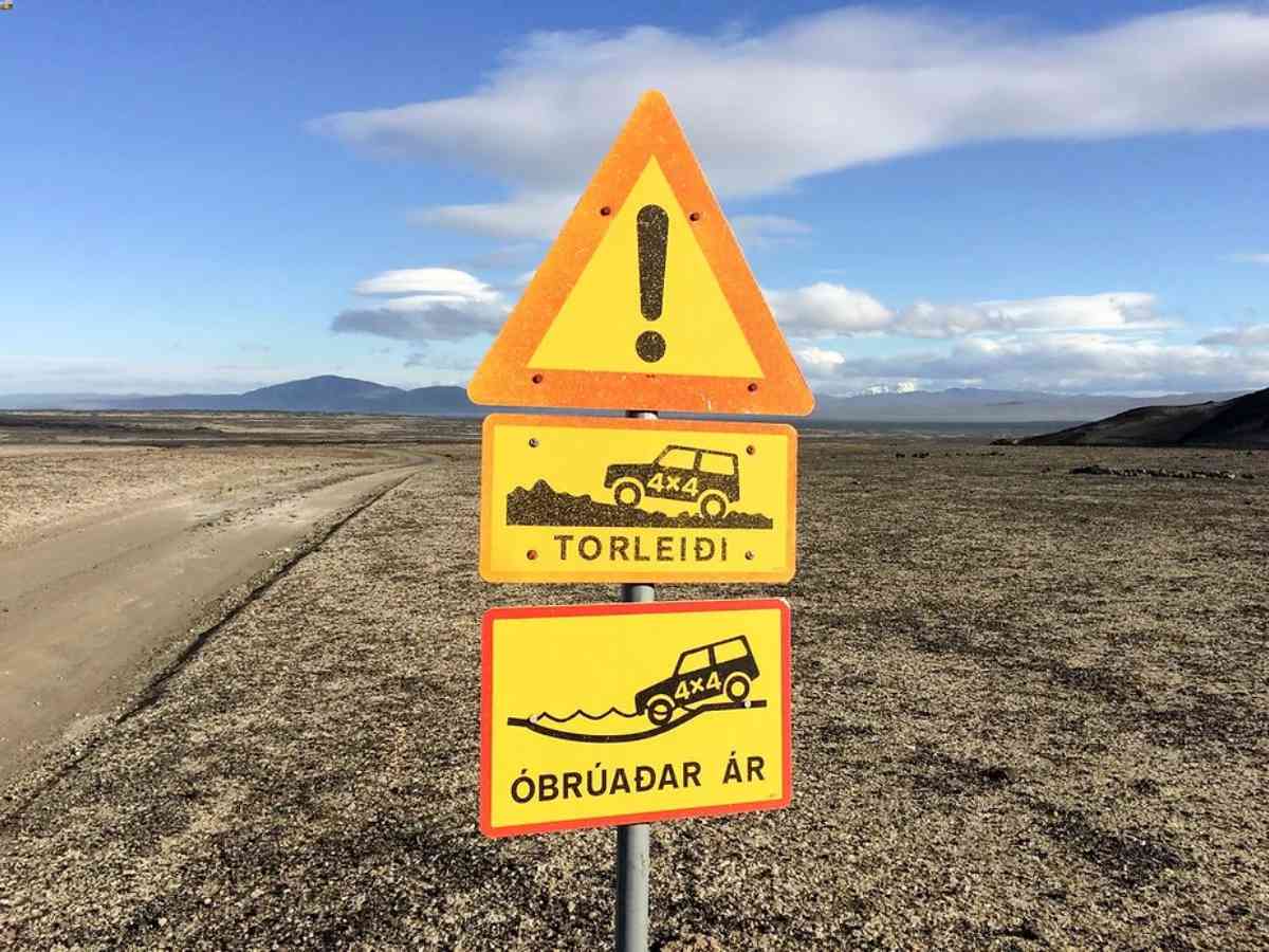 Warning signs in Iceland's highlands indicating difficult terrain and river crossings for 4x4 vehicles, set against a barren landscape and blue sky