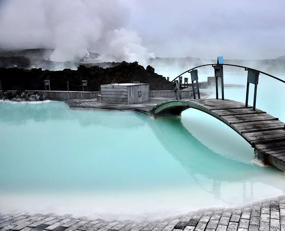 A serene view of the Blue Lagoon's geothermal waters in Iceland, with a wooden bridge crossing over the milky blue water and steam rising in the background