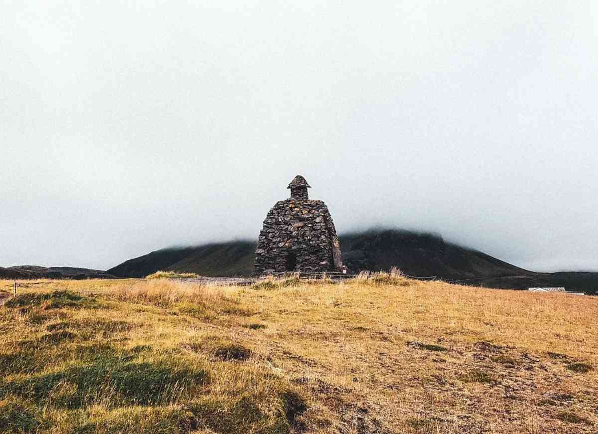 A stone cairn in an open field with mist-covered mountains in the background, located in Iceland