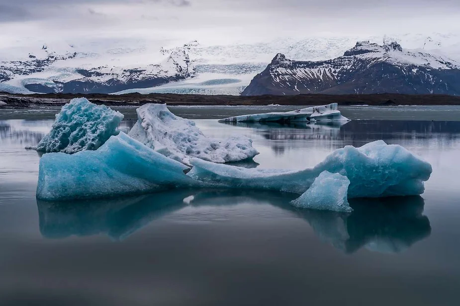 Floating icebergs in the Jökulsárlón Glacier Lagoon, Iceland, with a backdrop of snow-covered mountains and a glacier under a cloudy sky