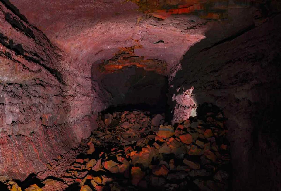 The interior of Vidgelmir Cave in Iceland, featuring rugged lava rock walls and floor, with dim lighting highlighting the cave’s volcanic formations and textures.