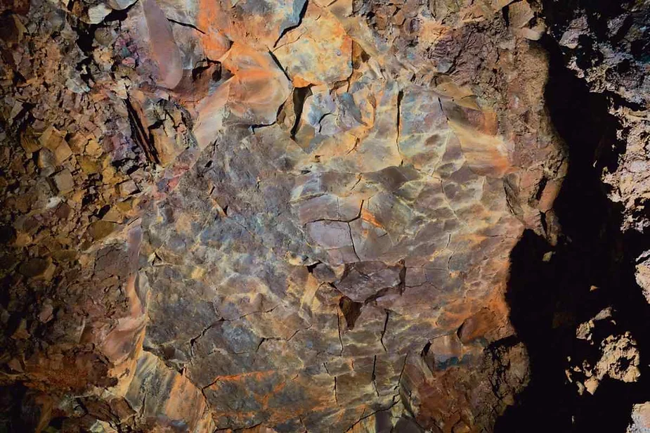 Close-up of colorful, textured lava rock formations inside Vidgelmir Cave in Iceland, showcasing the unique geological layers and vibrant hues of the cave's volcanic walls.